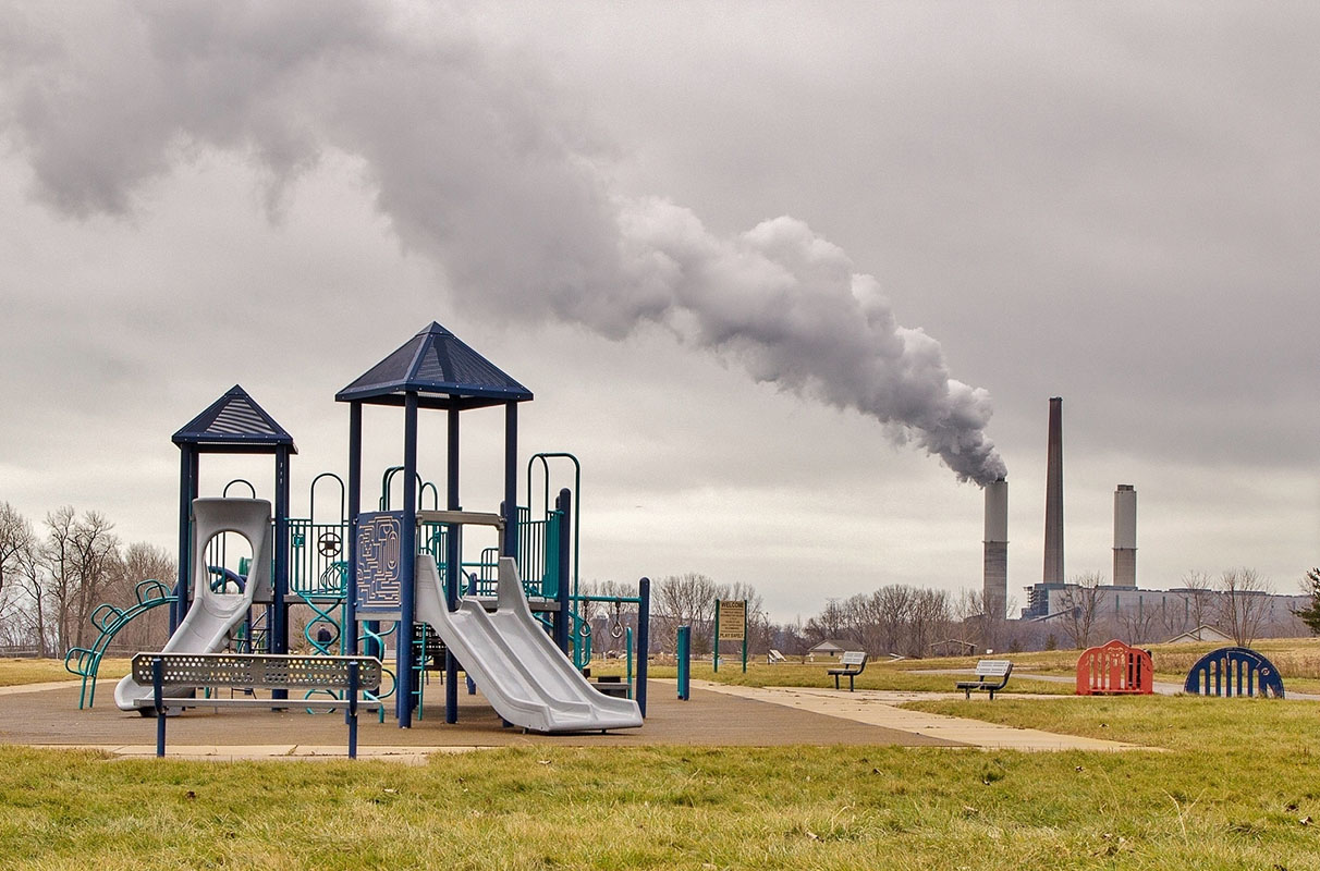 Childrens playground with a smokestack billowing smoke in the background.